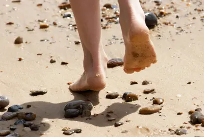 Dziecko z gołymi stopami biegnie po piasku. Chodzenie na boso zapobiega przed pojawieniem się płaskostopia u dzieci.